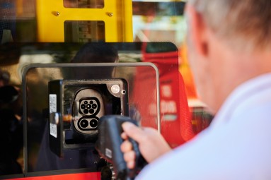 A person holds a charging plug and points it at the socket of a battery-electric bus. 