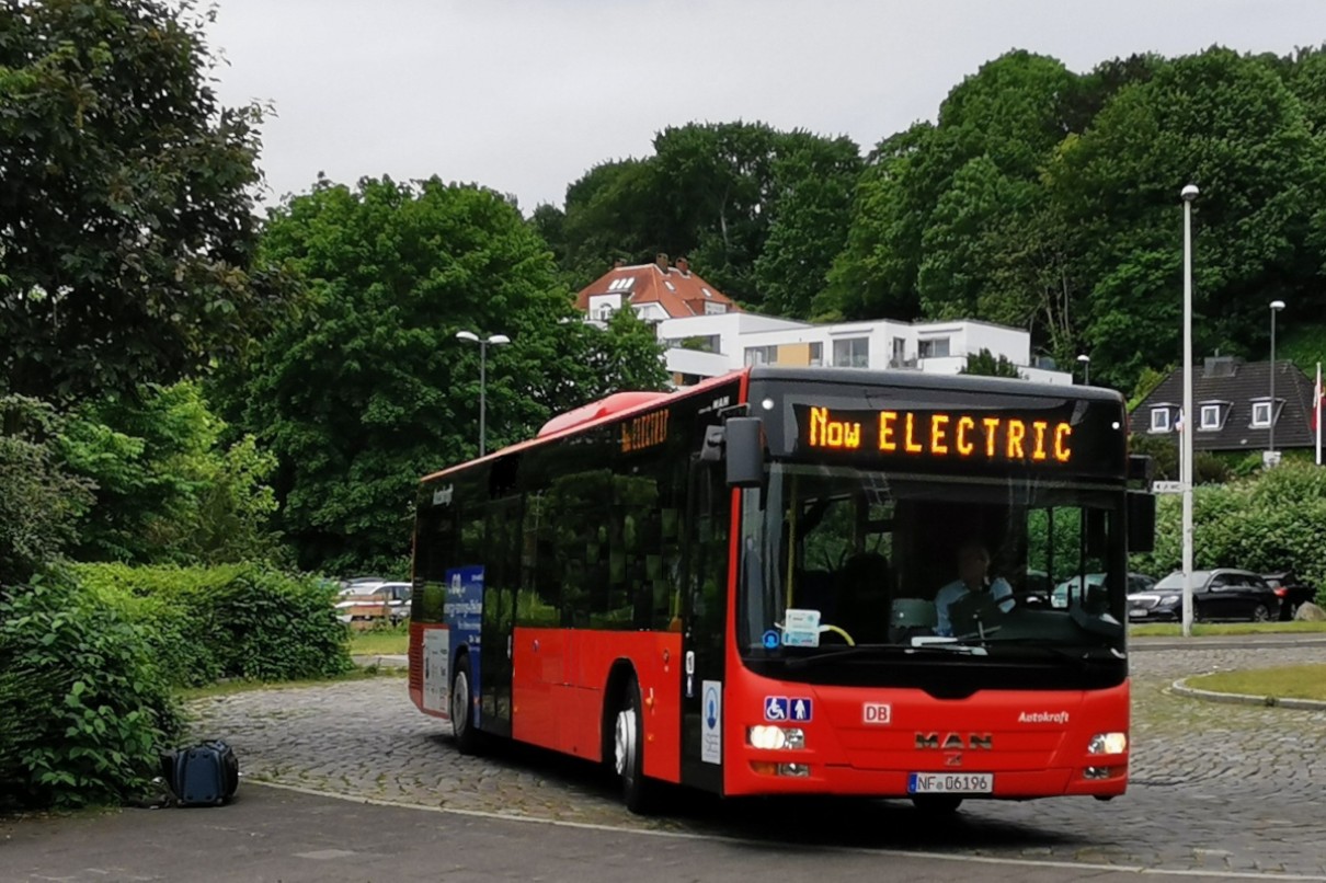 Ein umgerüsteter, roter MAN-Dieselbus der DB-Regio-Tochter Autokraft im Einsatz. Auf der Außenanzeige ist „Now Electric“ zu lesen. 